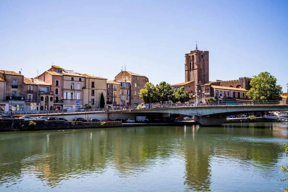 La cathédrale Saint-Étienne et les maisons des quais d’Agde se reflètent dans l’Hérault, sous un ciel d’été