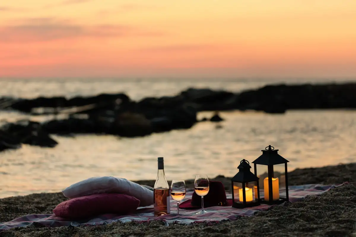 Deux verres de rosé, des coussins et des lanternes posés sur une plage au coucher du soleil