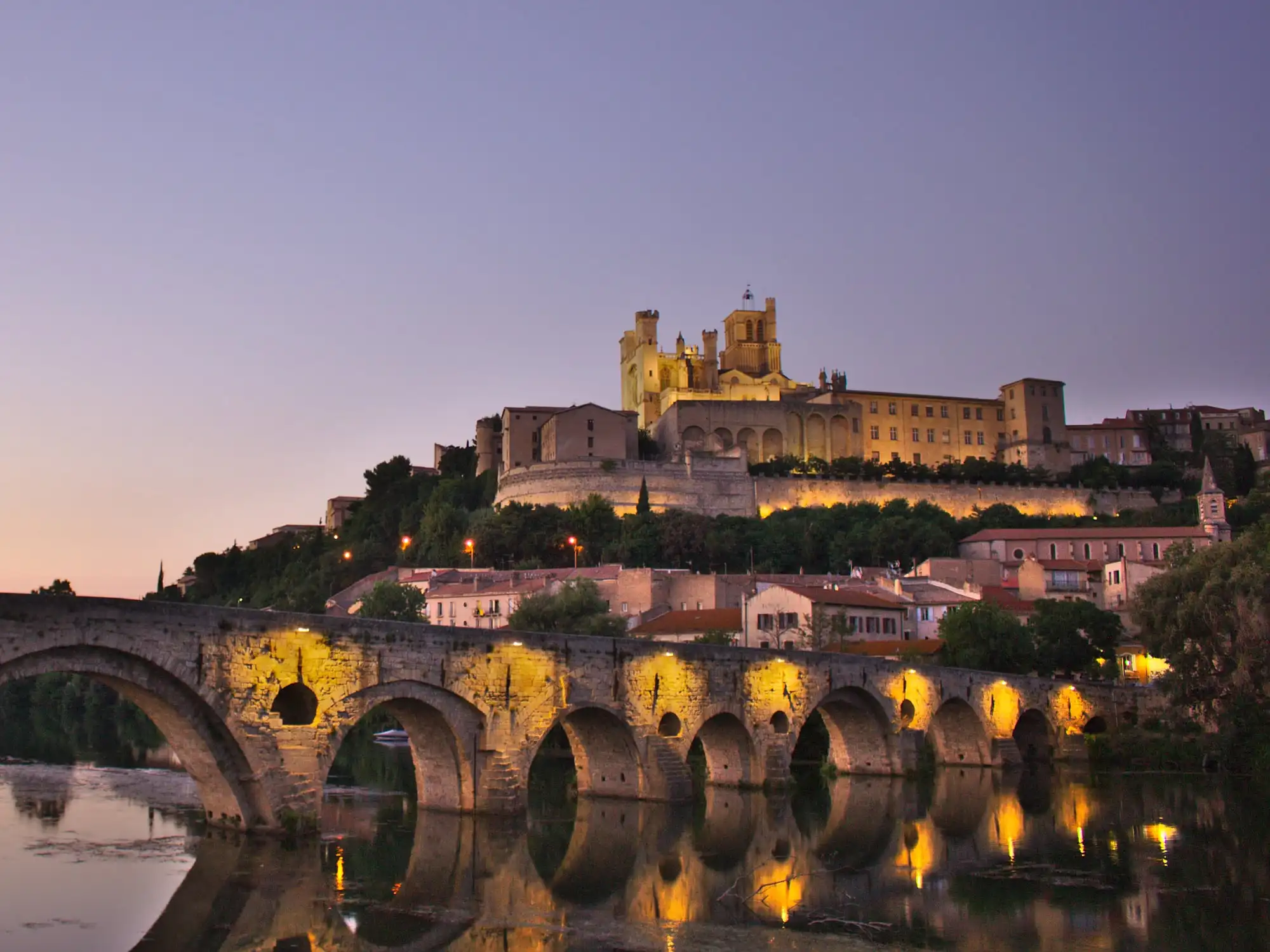 La cathédrale Saint-Nazaire de Béziers éclairée au crépuscule, au-dessus du Pont-Vieux et de l’Orb