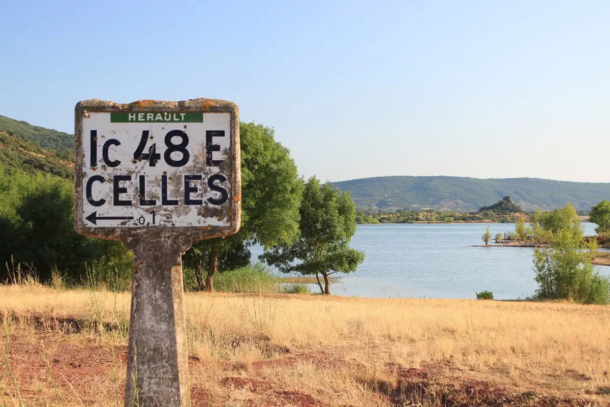 Une ancienne borne routière au bord d’un lac, devant des collines boisées