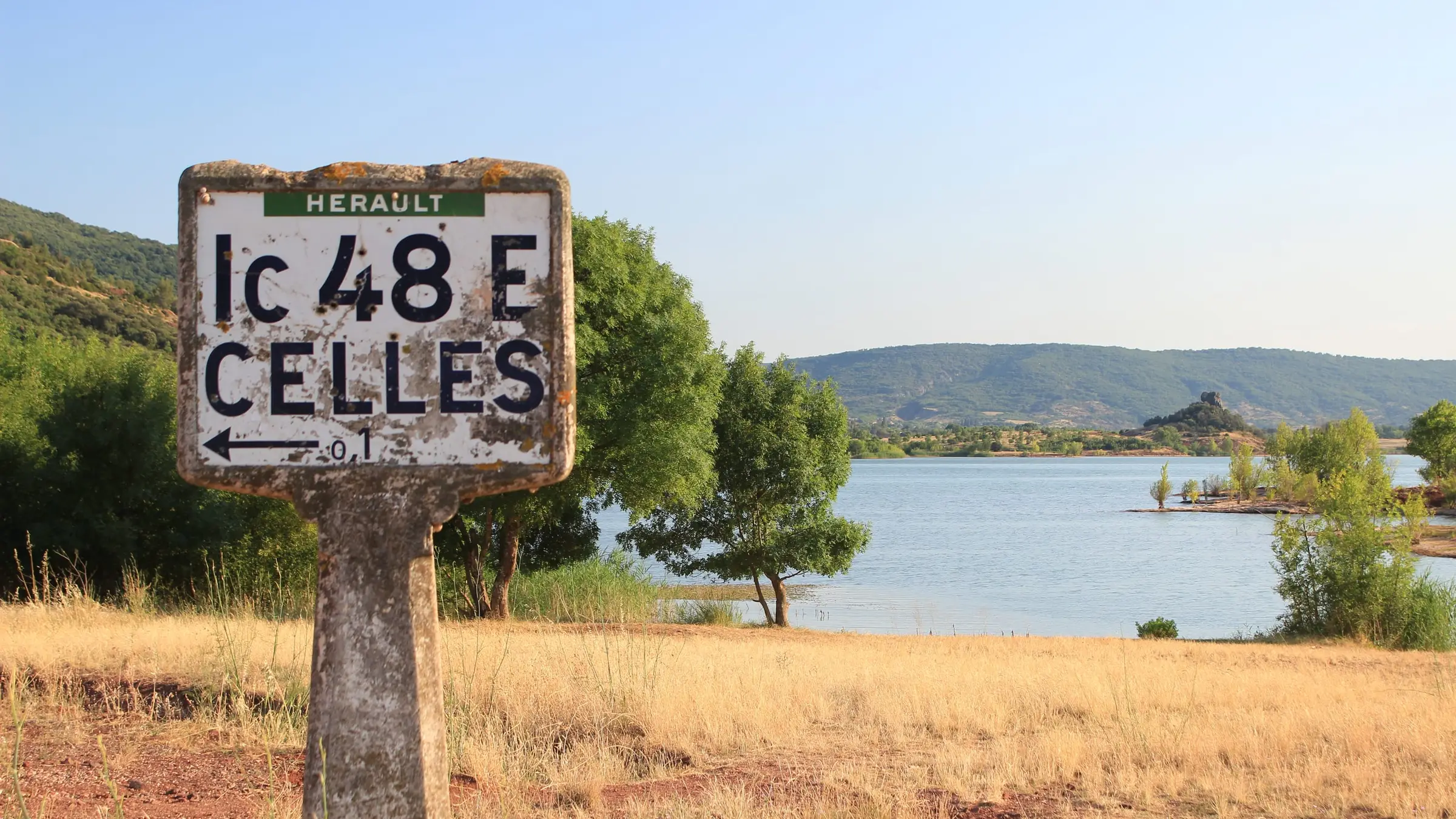 Une ancienne borne routière au bord d’un lac, devant des collines boisées
