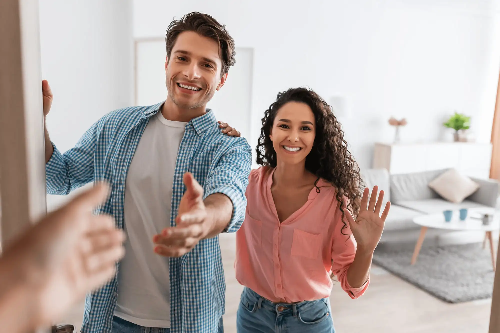 Un couple souriant accueille ses invités sur le pas de la porte