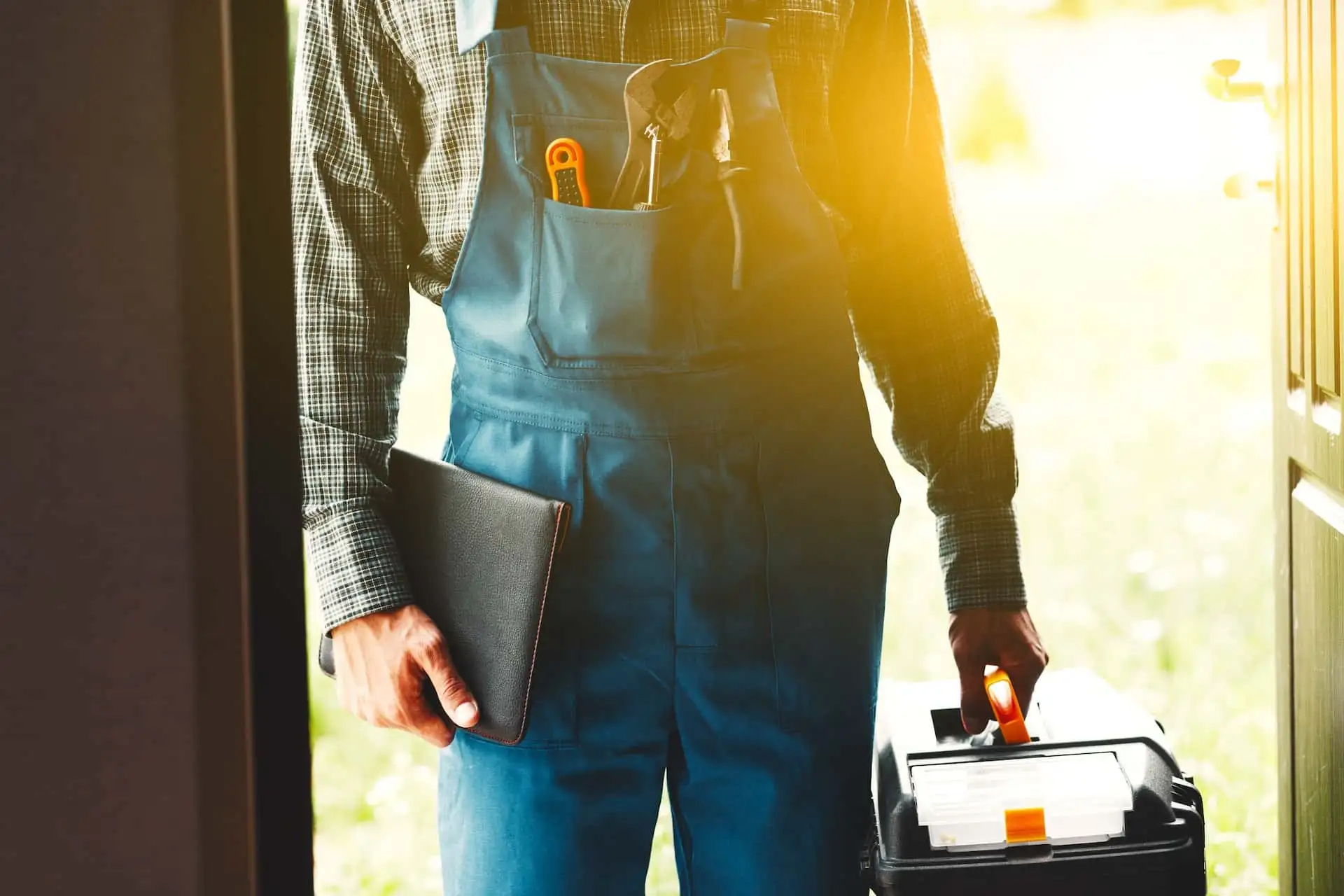 Un technicien en salopette, caisse à outils à la main, sur le pas de la porte