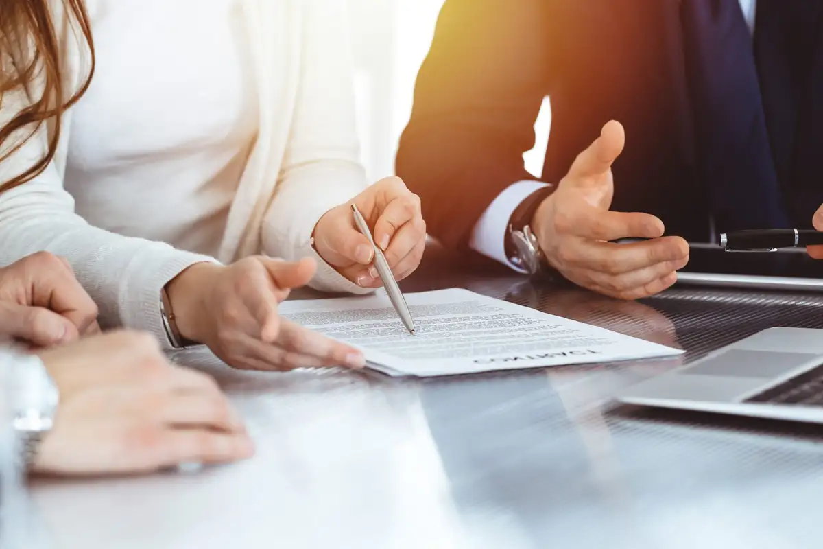 Hands around a table in the sunlight, a pen pointing to a document during a meeting
