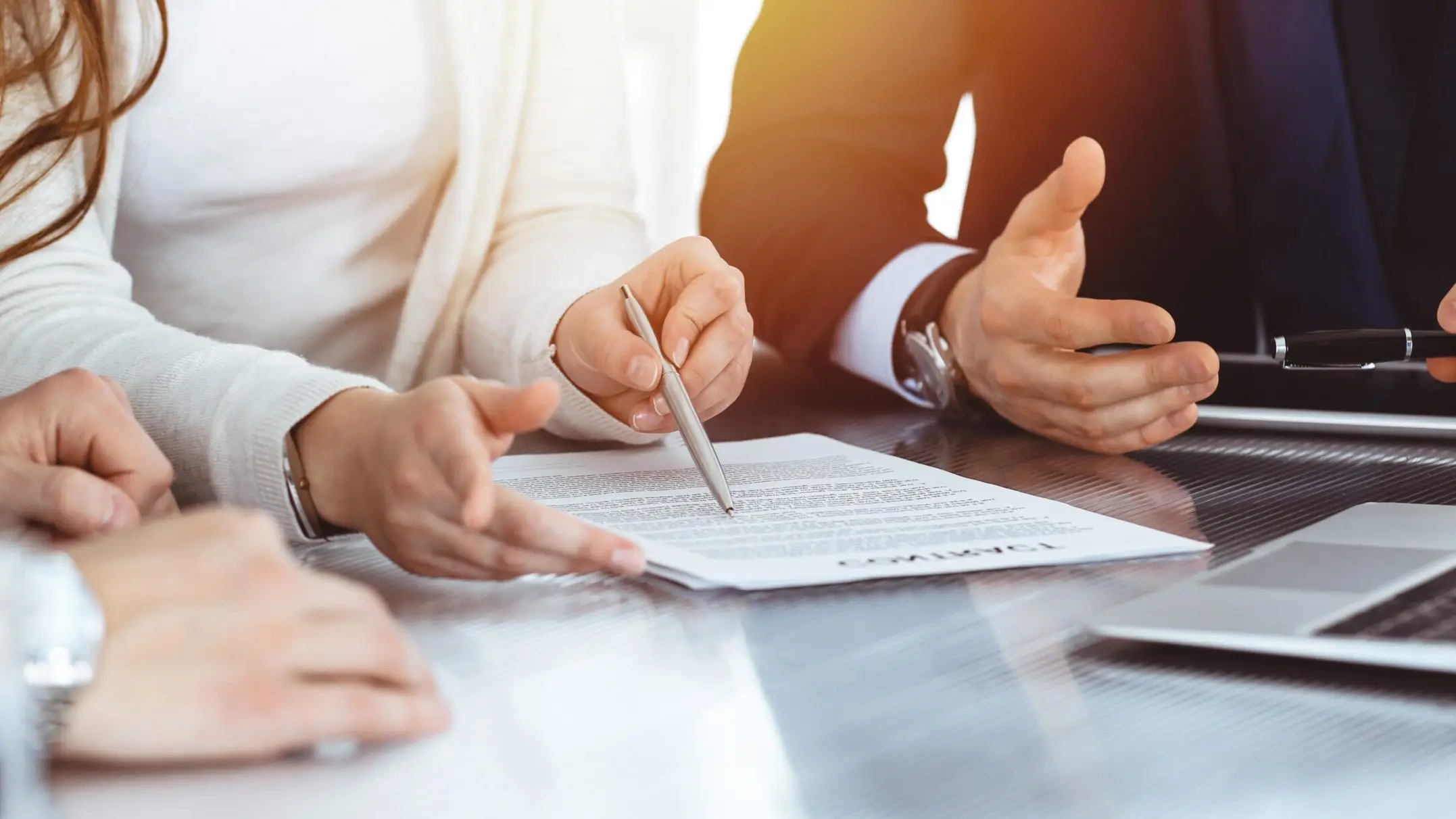 Hands around a table in the sunlight, a pen pointing to a document during a meeting
