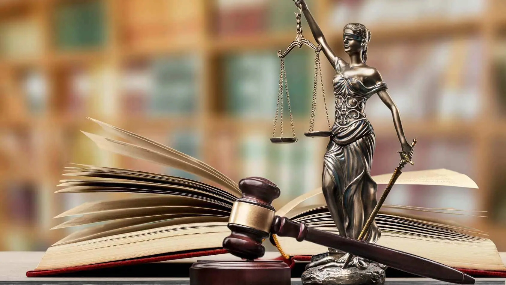 Statue de la Justice tenant sa balance, un marteau de juge et un livre de droit ouvert sur un bureau