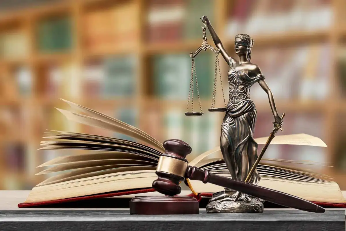 Statue de la Justice tenant sa balance, un marteau de juge et un livre de droit ouvert sur un bureau