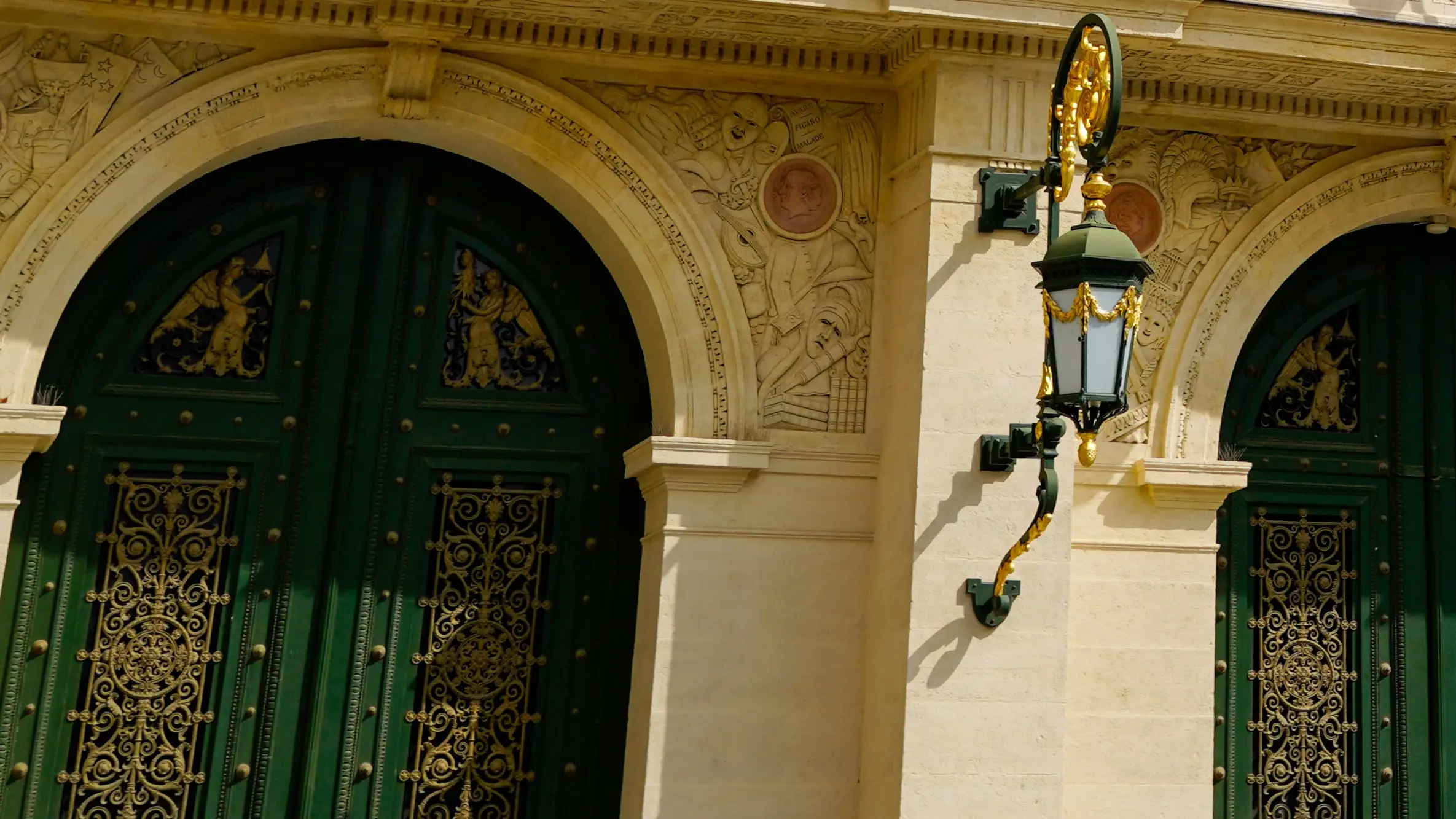 Hautes portes vertes à ferronneries dorées sous des arches de pierre sculptée, et une lanterne en fer forgé