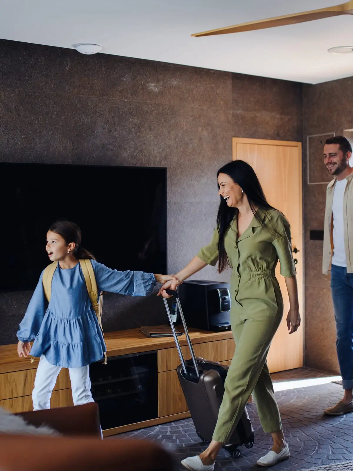 Une famille, valise à la main, entre en souriant dans sa maison de vacances