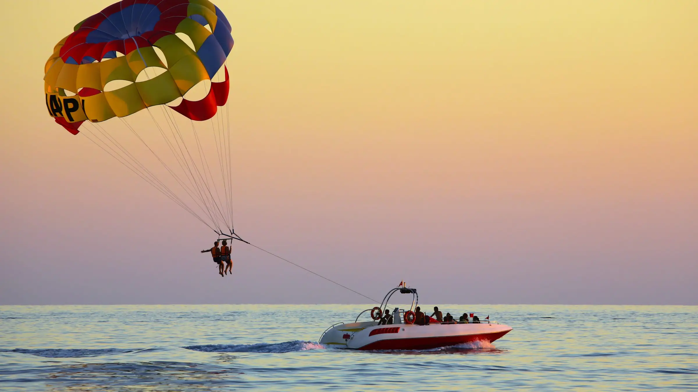 Un parachute ascensionnel tiré par un bateau sur une mer calme, dans la lumière dorée du coucher du soleil