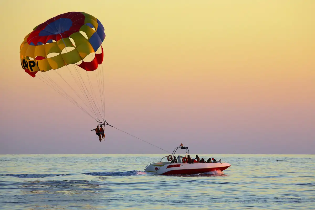 Un parachute ascensionnel tiré par un bateau sur une mer calme, dans la lumière dorée du coucher du soleil