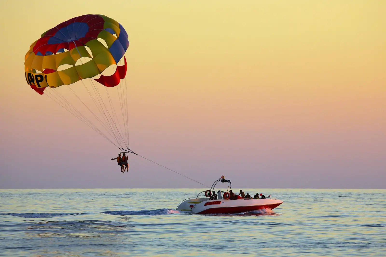 Un parachute ascensionnel tiré par un bateau sur une mer calme, dans la lumière dorée du coucher du soleil