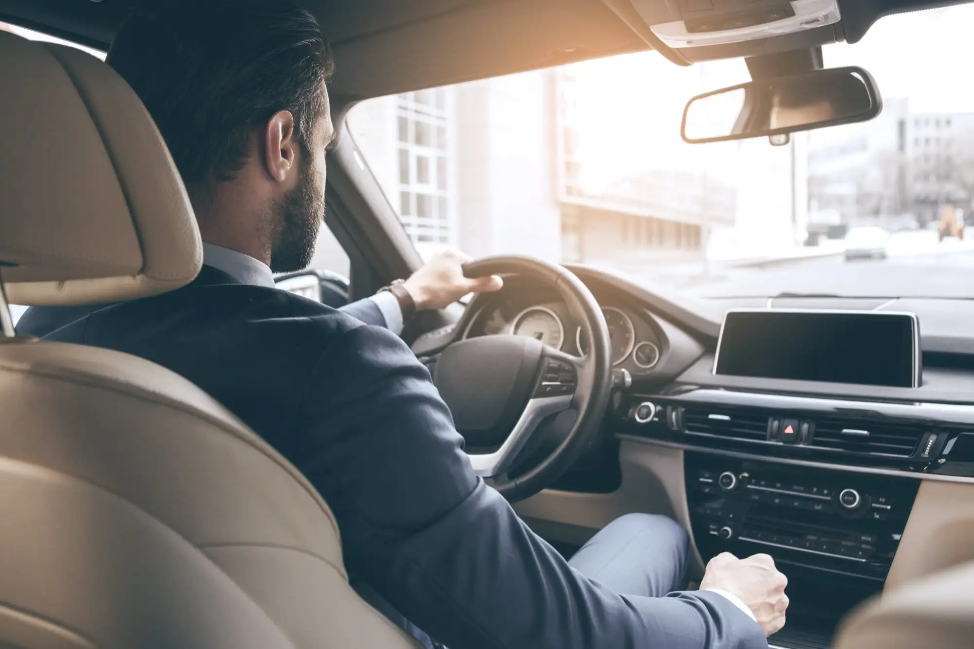 Chauffeur en costume au volant d’une berline, vu depuis la banquette arrière