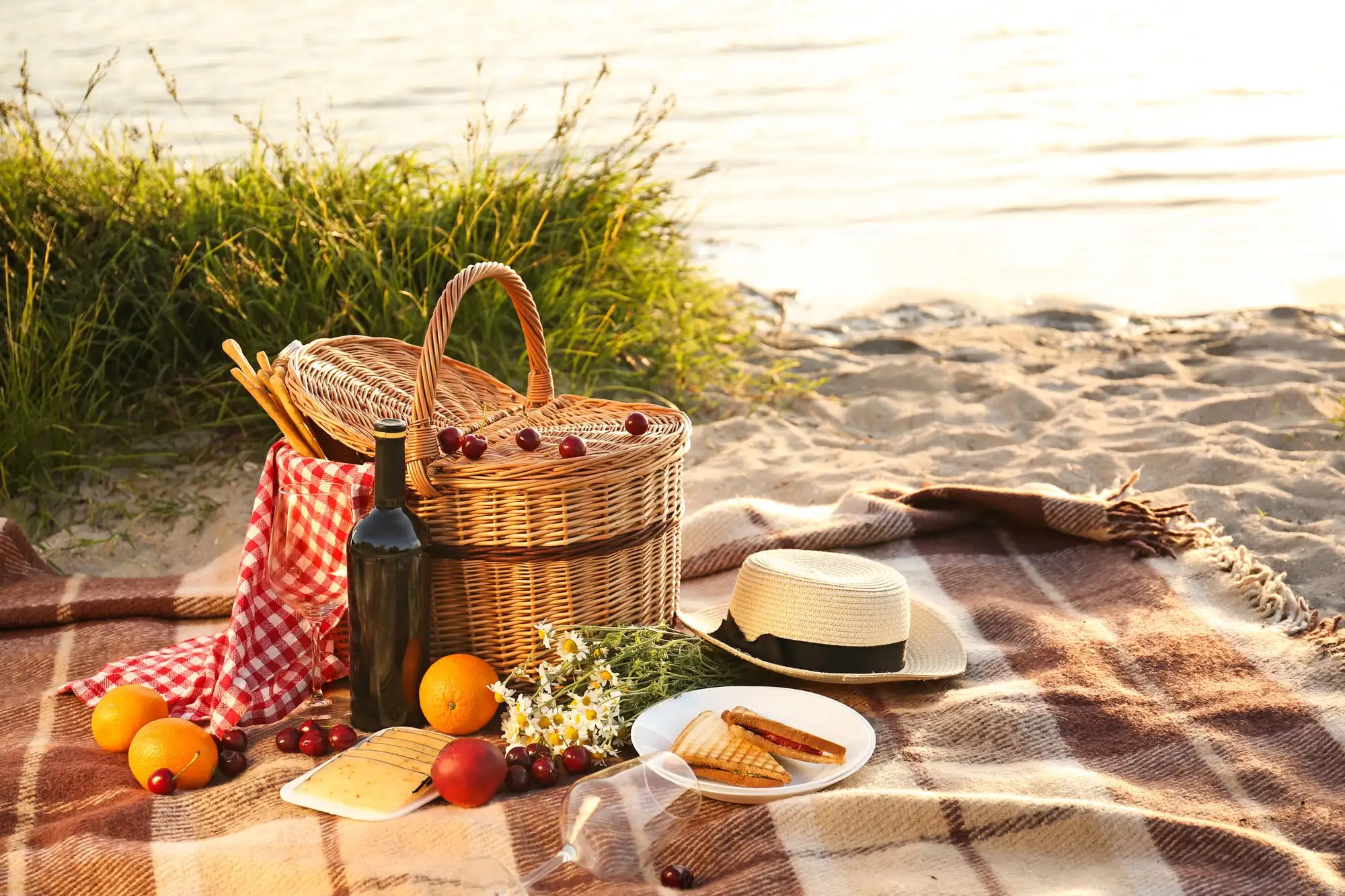 Panier pique-nique en osier, fruits et sandwichs sur un plaid au bord de l’eau