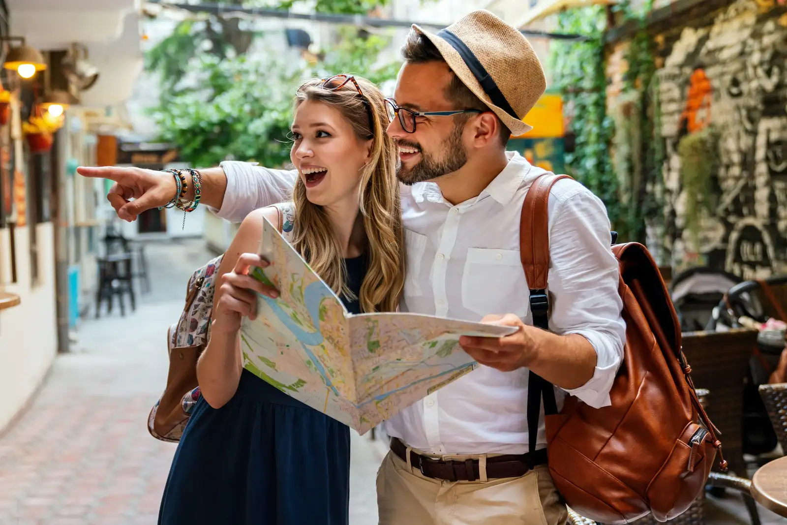 Un couple de voyageurs consulte une carte dépliée et montre du doigt la direction, dans une ruelle ensoleillée