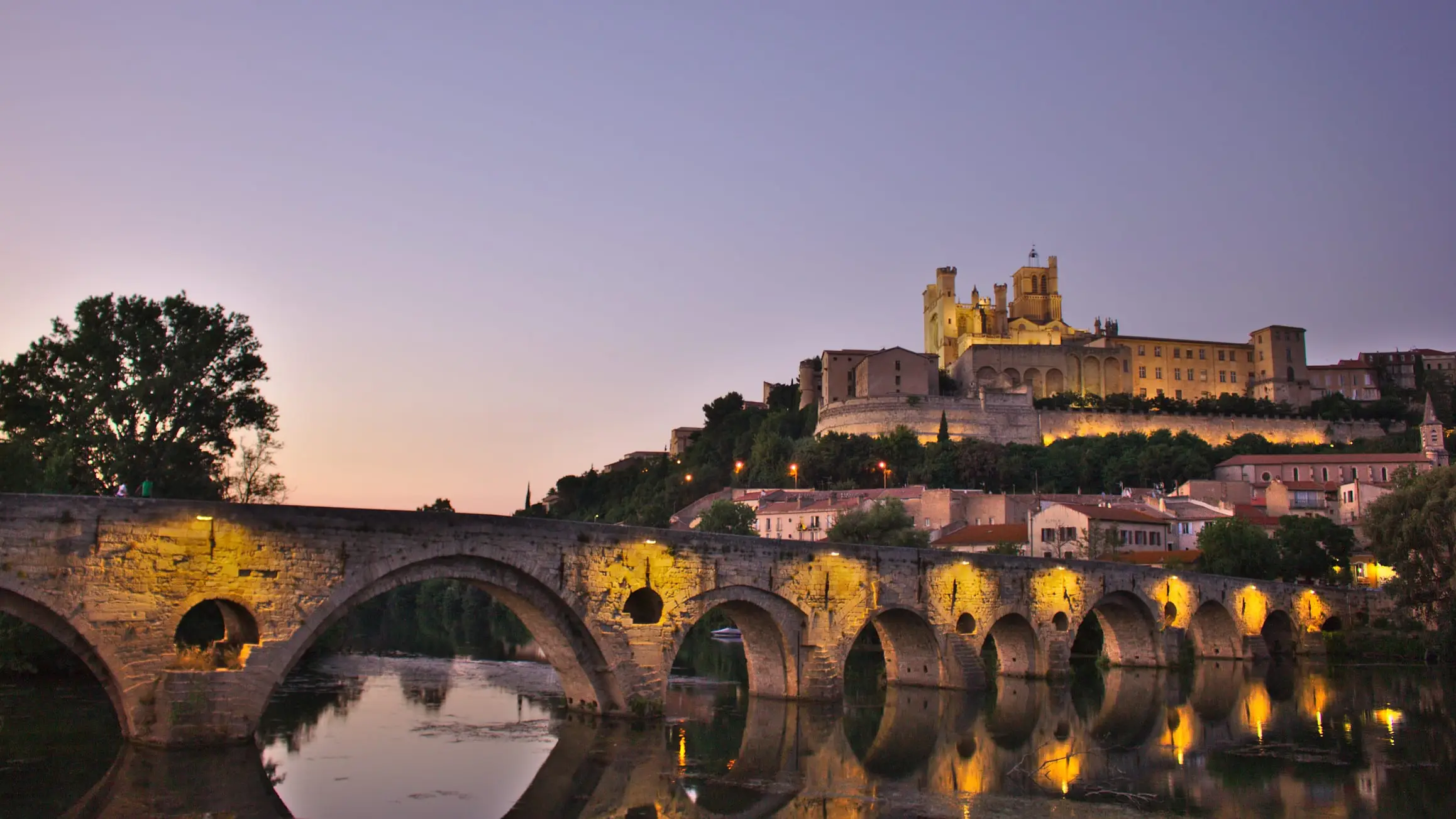 À la tombée du jour, la cathédrale Saint-Nazaire domine l’Orb et les arches éclairées du Pont-Vieux, à Béziers