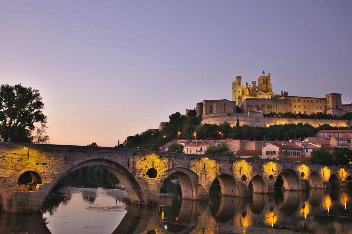 À la tombée du jour, la cathédrale Saint-Nazaire domine l’Orb et les arches éclairées du Pont-Vieux, à Béziers